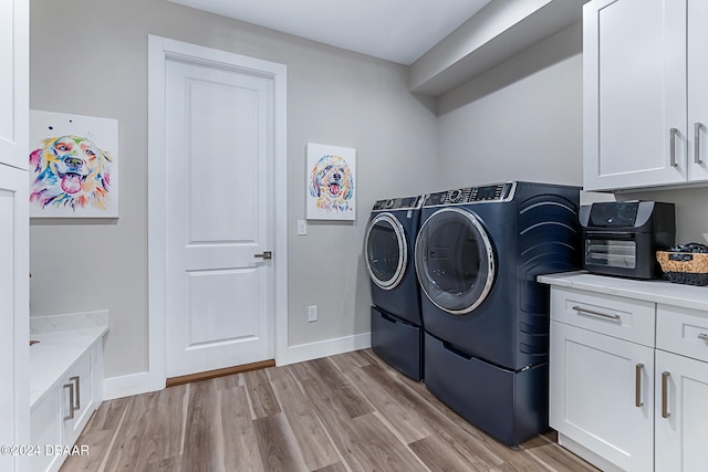 laundry area featuring washer and clothes dryer, light hardwood / wood-style floors, and cabinets