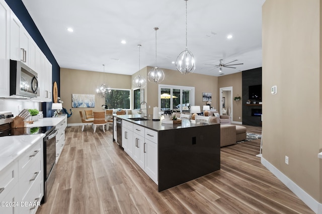 kitchen with ceiling fan with notable chandelier, stainless steel appliances, sink, decorative light fixtures, and a center island with sink