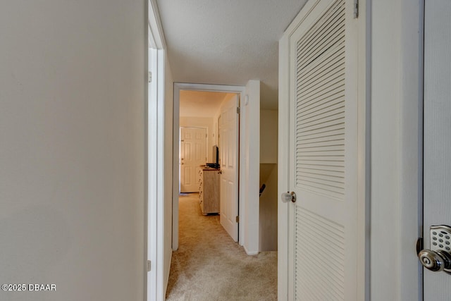 hallway featuring light colored carpet and a textured ceiling