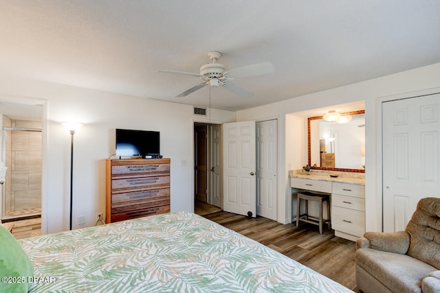 bedroom featuring ceiling fan, ensuite bathroom, dark hardwood / wood-style flooring, and two closets