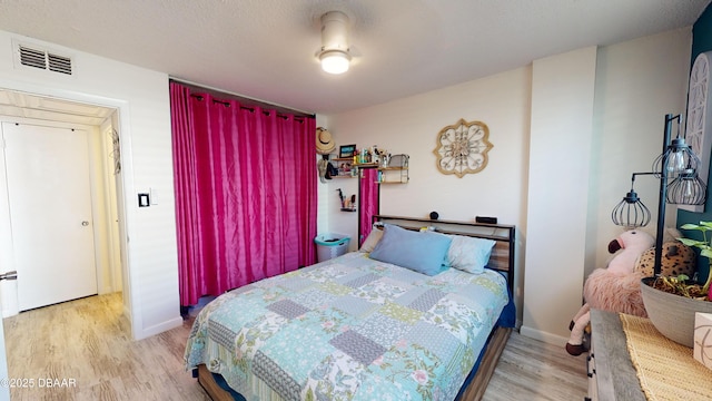 bedroom with light wood finished floors, baseboards, visible vents, and a textured ceiling