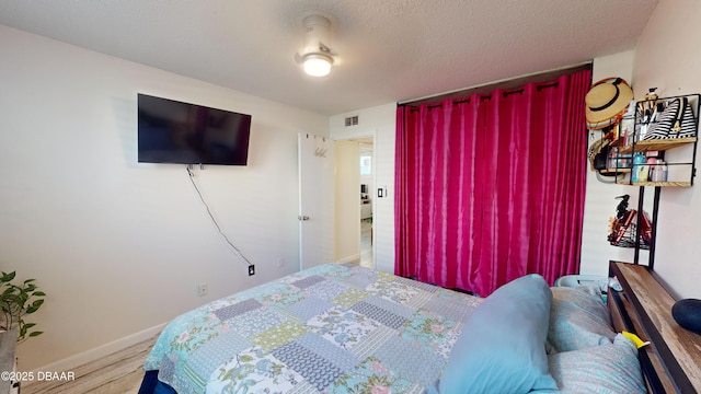 bedroom with a textured ceiling, wood finished floors, visible vents, and baseboards