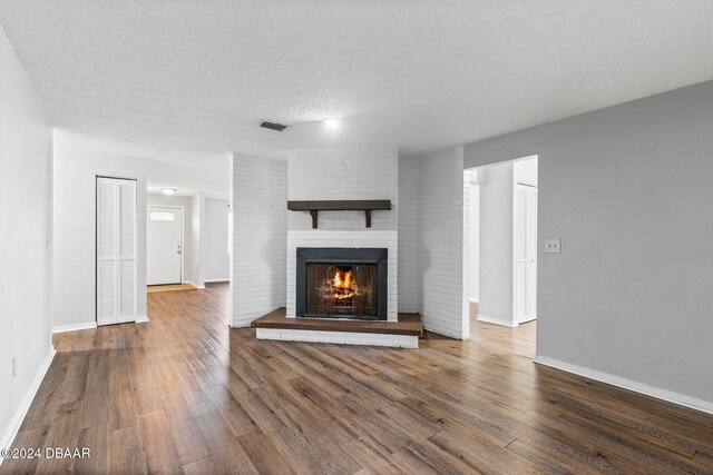 unfurnished living room featuring a textured ceiling, a brick fireplace, and dark wood-type flooring