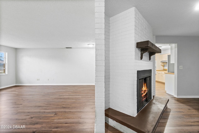 unfurnished living room with a fireplace, dark wood-type flooring, and a textured ceiling