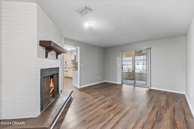 unfurnished living room with dark hardwood / wood-style flooring, a textured ceiling, and a brick fireplace