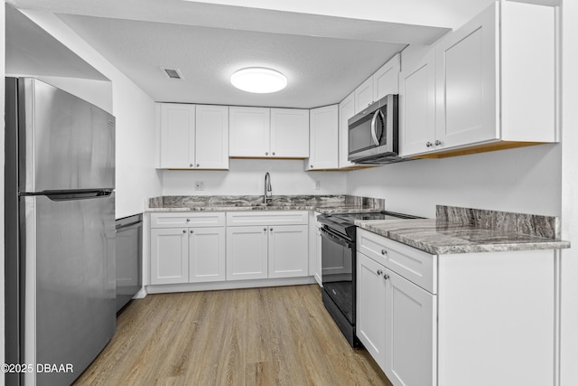 kitchen with visible vents, a sink, stainless steel appliances, light wood-style floors, and white cabinetry