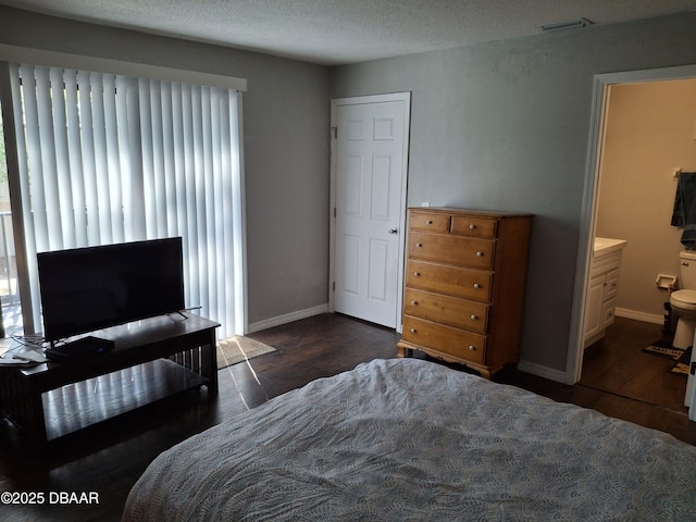 bedroom featuring a textured ceiling, ensuite bathroom, dark wood-style flooring, visible vents, and baseboards