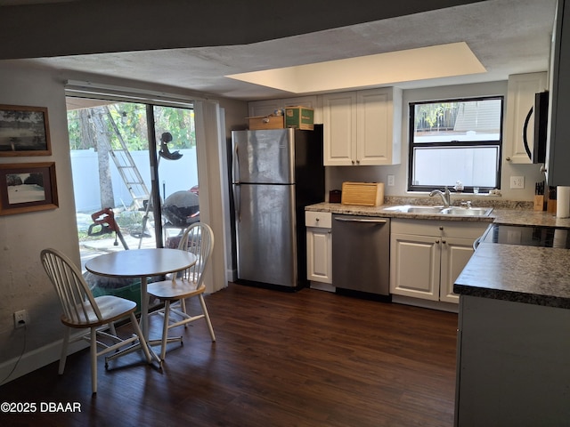 kitchen with appliances with stainless steel finishes, white cabinetry, a sink, and dark wood-style floors