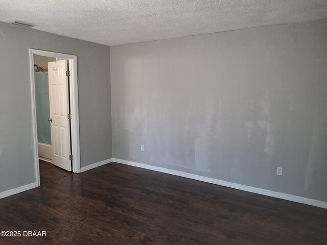 unfurnished room with dark wood-type flooring, a textured ceiling, visible vents, and baseboards