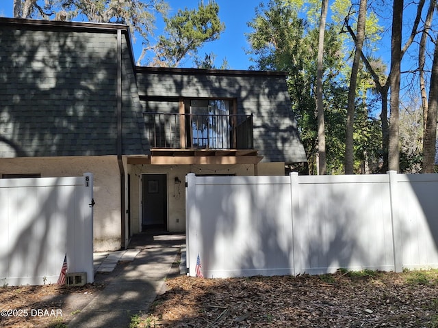 view of front of property with mansard roof, a balcony, a shingled roof, fence, and stucco siding