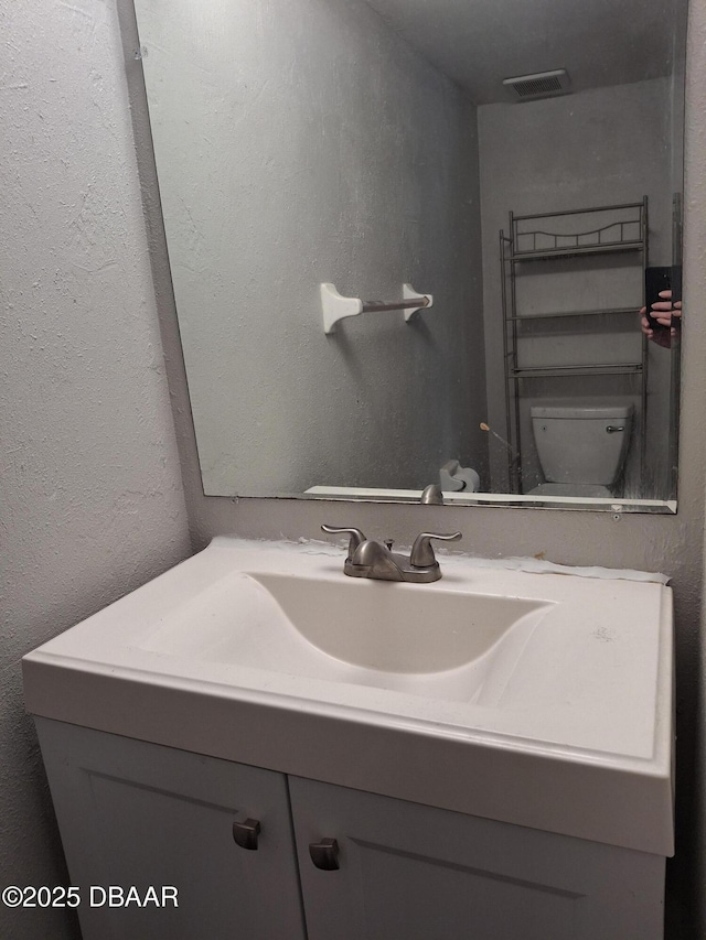 bathroom with visible vents, a textured wall, vanity, and toilet