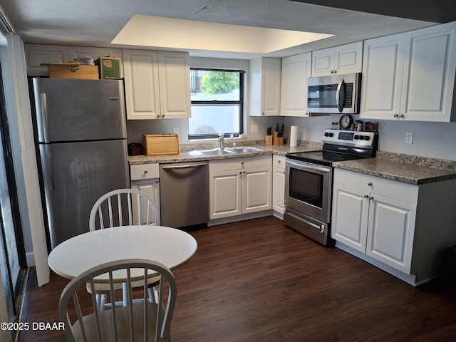 kitchen with stainless steel appliances, stone countertops, dark wood-type flooring, white cabinetry, and a sink