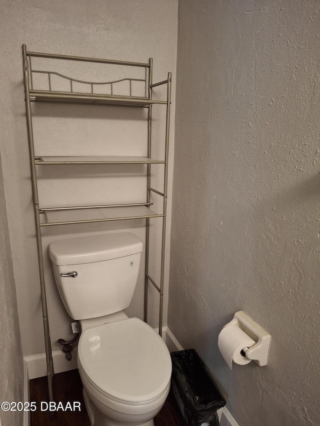 bathroom featuring baseboards, a textured wall, and toilet