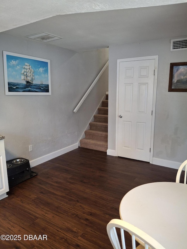 interior space featuring dark wood-style flooring, visible vents, stairway, and baseboards