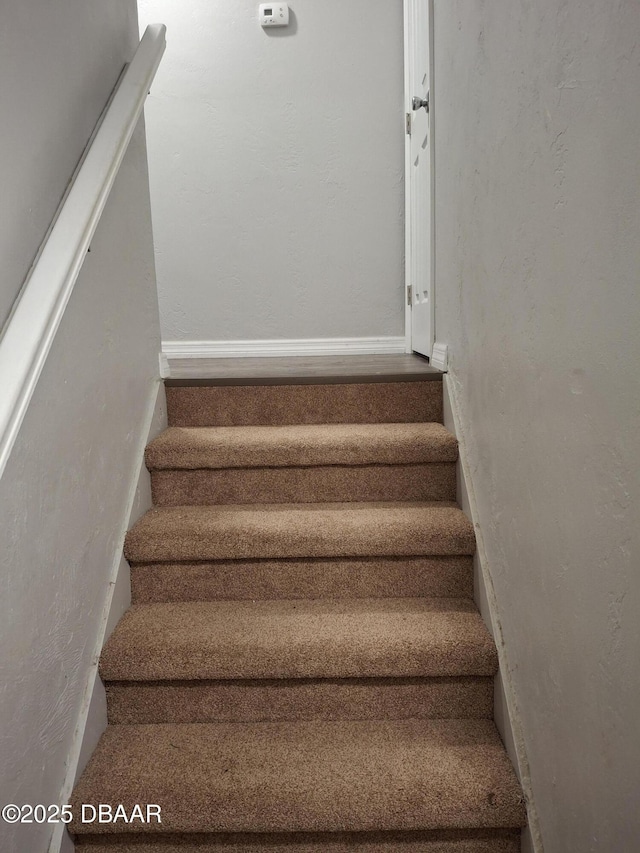 staircase with a textured wall and baseboards