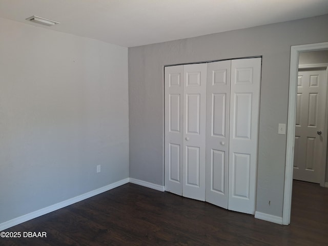 unfurnished bedroom featuring baseboards, visible vents, a closet, and dark wood finished floors