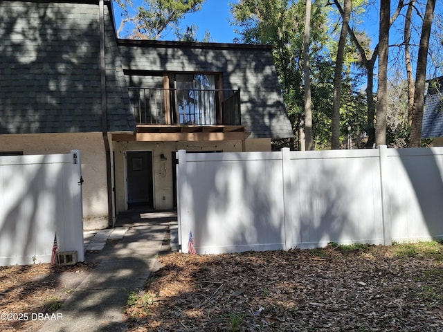 exterior space with mansard roof, a shingled roof, stucco siding, fence, and a balcony