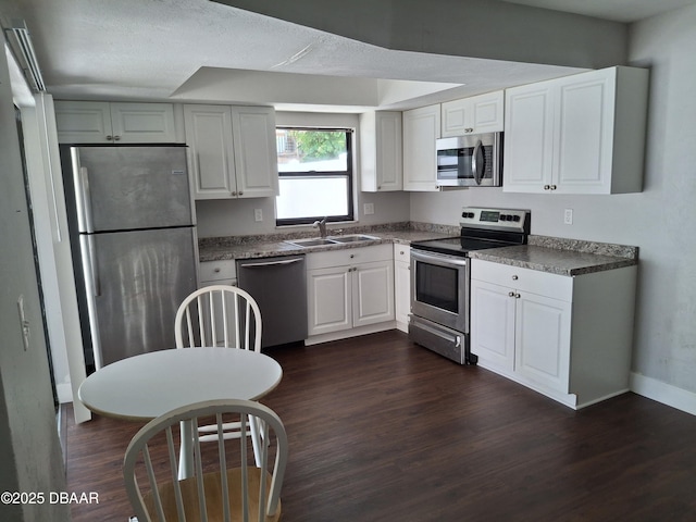 kitchen featuring stainless steel appliances, dark wood-style floors, a sink, and dark countertops