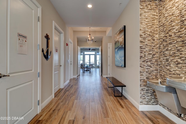 corridor with a chandelier, light wood-type flooring, and baseboards