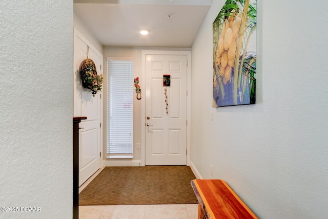 entryway featuring light carpet, a textured wall, baseboards, and light tile patterned flooring