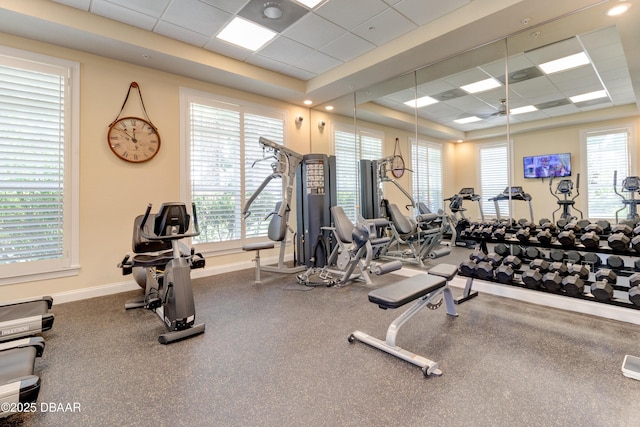 exercise room featuring a tray ceiling, baseboards, a drop ceiling, and a wealth of natural light