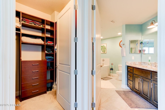 bathroom featuring baseboards, toilet, tile patterned floors, a walk in closet, and vanity