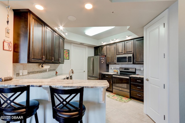 kitchen featuring a peninsula, dark brown cabinetry, a kitchen bar, and appliances with stainless steel finishes