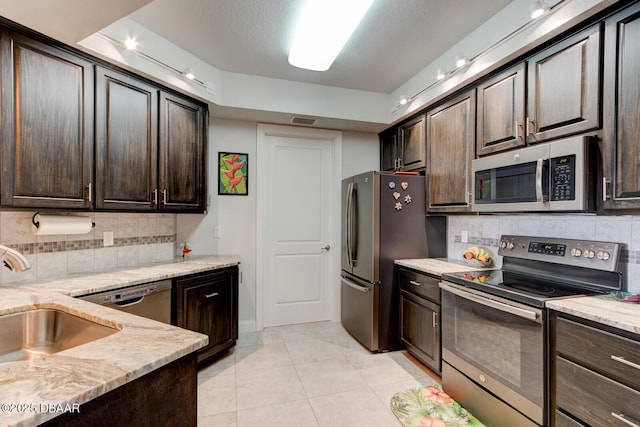 kitchen with appliances with stainless steel finishes, a sink, light stone counters, and dark brown cabinets