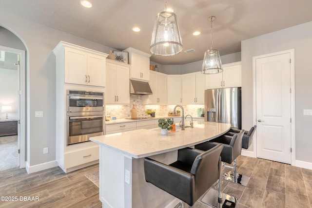 557 Mosaic Blvd, Daytona Beach, FL 32124 - kitchen featuring stainless steel appliances, under cabinet range hood, light wood-style floors, white cabinetry, and an island with sink