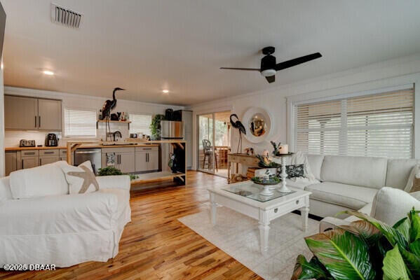 living room with crown molding, ceiling fan, sink, and light wood-type flooring