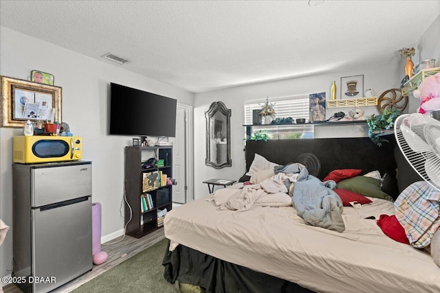 bedroom featuring a textured ceiling, visible vents, and freestanding refrigerator