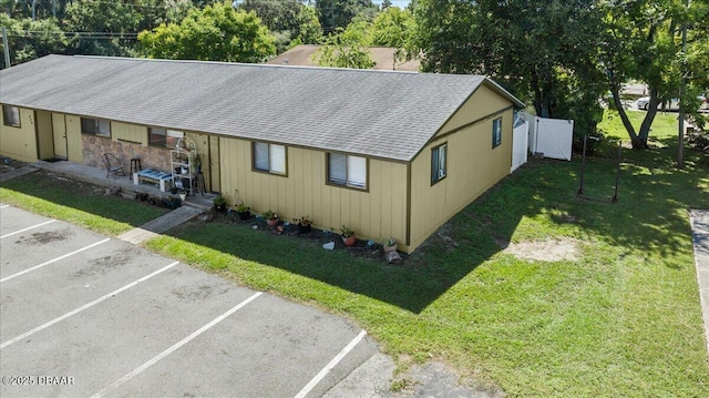 exterior space with roof with shingles, uncovered parking, and a front yard