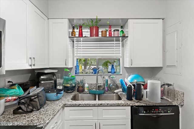 kitchen with black dishwasher, light stone counters, a sink, and white cabinetry