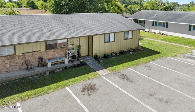 view of front of house featuring stone siding, a shingled roof, uncovered parking, and a front lawn