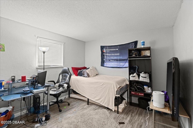 bedroom featuring a textured ceiling, baseboards, wood finished floors, and a textured wall