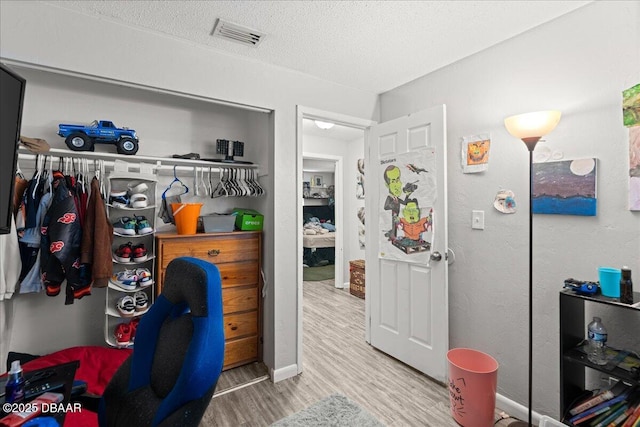 interior space featuring a textured ceiling, wood finished floors, visible vents, baseboards, and a closet