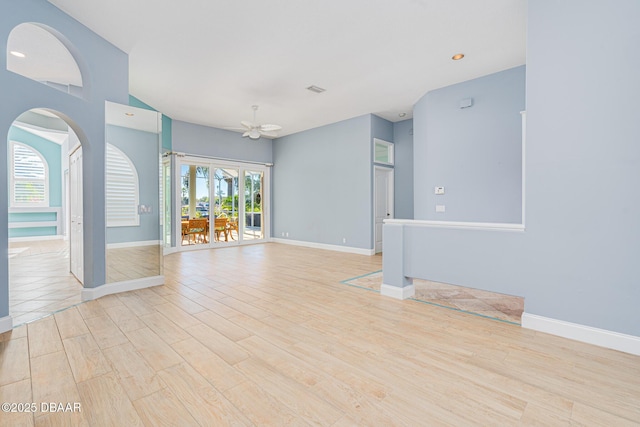 unfurnished room with light wood finished floors, ceiling fan, visible vents, baseboards, and arched walkways