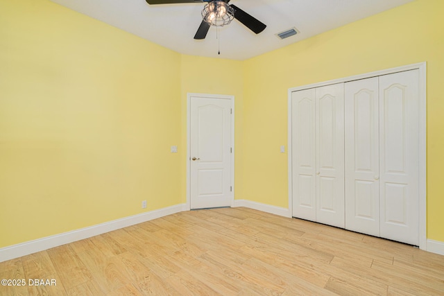 unfurnished bedroom with a closet, ceiling fan, light wood finished floors, baseboards, and visible vents