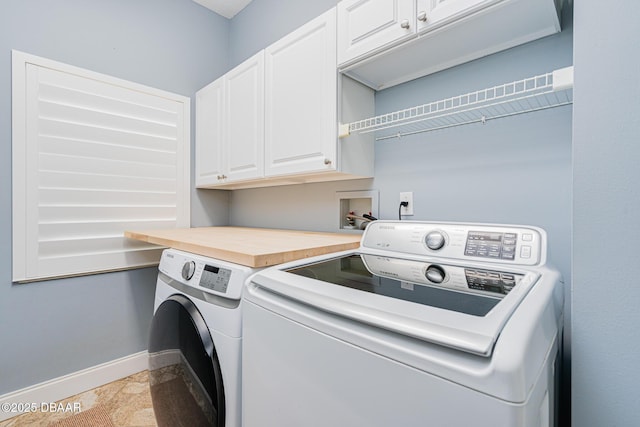 clothes washing area featuring stone finish floor, independent washer and dryer, cabinet space, and baseboards