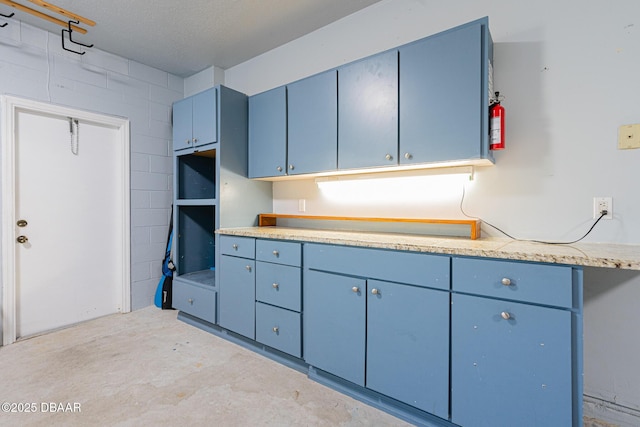 kitchen with light countertops, blue cabinetry, and unfinished concrete flooring