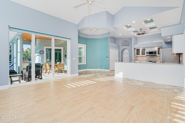unfurnished living room with baseboards, a ceiling fan, a high ceiling, and light wood-style flooring