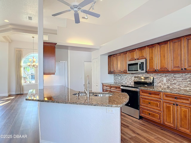 kitchen featuring sink, hardwood / wood-style flooring, appliances with stainless steel finishes, dark stone countertops, and decorative backsplash