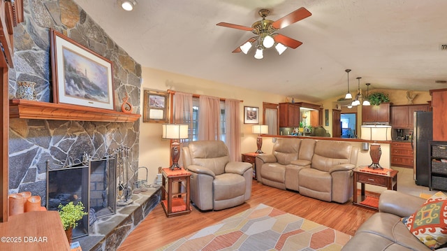 living area with a ceiling fan, light wood-style flooring, vaulted ceiling, and a stone fireplace