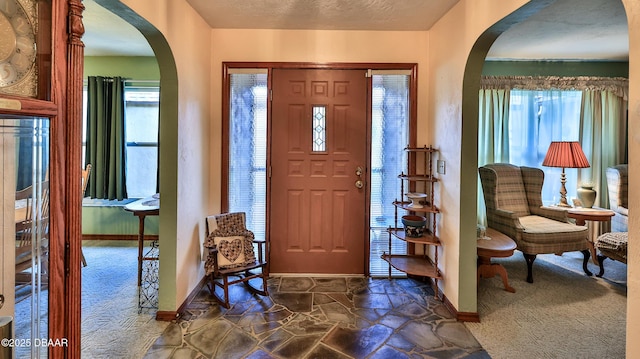 entryway with dark colored carpet, arched walkways, and baseboards