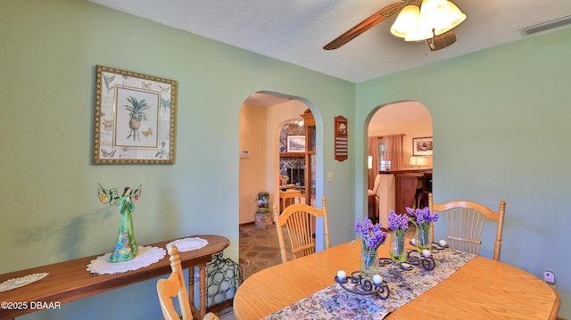dining room with arched walkways, stone finish floor, a ceiling fan, and visible vents