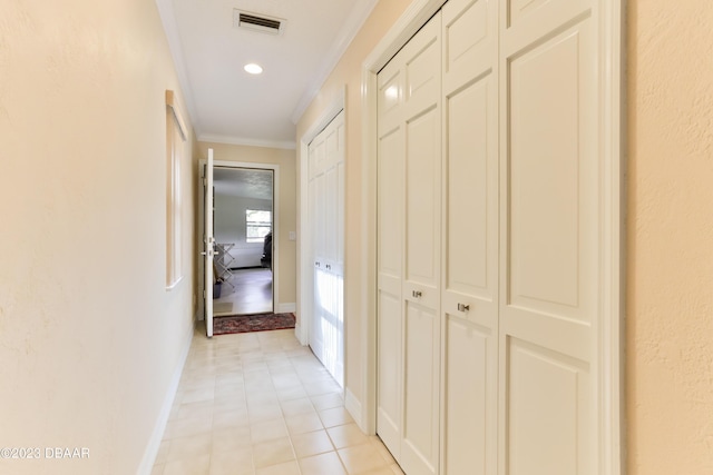 hall with light tile patterned floors, baseboards, visible vents, and ornamental molding