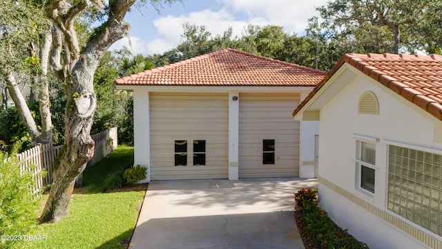 exterior space featuring a detached garage, an outbuilding, a tiled roof, fence, and a front yard