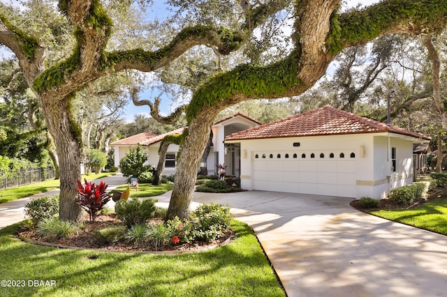 mediterranean / spanish house featuring concrete driveway, a tiled roof, an attached garage, fence, and stucco siding