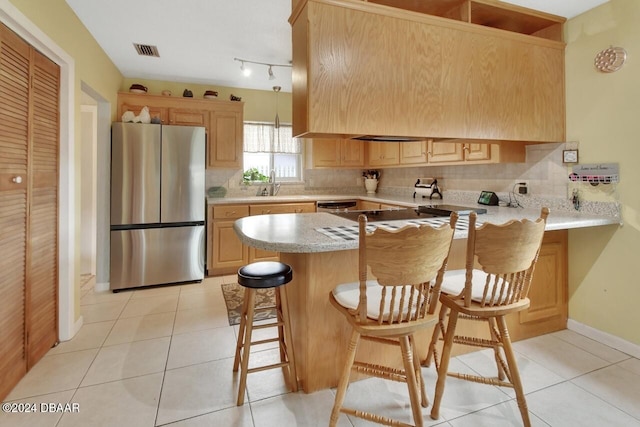 kitchen featuring kitchen peninsula, stainless steel fridge, a kitchen bar, sink, and light tile patterned flooring