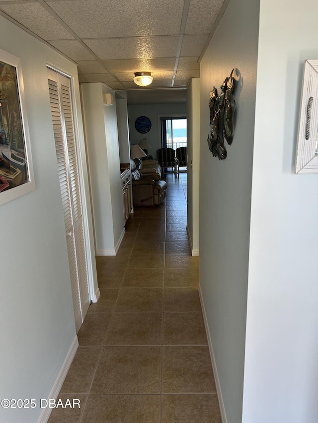 hallway with dark tile patterned flooring, baseboards, and a drop ceiling
